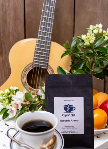 Cup N' Clef Acoustic Aroma coffee bag alongside a cup of coffee, a guitar, and fresh flowers, illustrating a relaxing and artistic coffee experience.