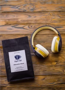 Cup N' Clef Alternative Roast coffee bag on a wooden table next to vintage yellow headphones, blending music and coffee culture.