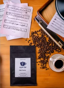 Folk Fusion coffee bag placed on a wooden table surrounded by sheet music and coffee beans, evoking a sense of creativity and rich flavor.