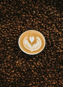 Top view of a freshly brewed latte with heart-shaped latte art, surrounded by roasted coffee beans